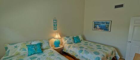 A room with two beds, each with matching blue and green bedding, a bedside lamp, and a small wall decoration.