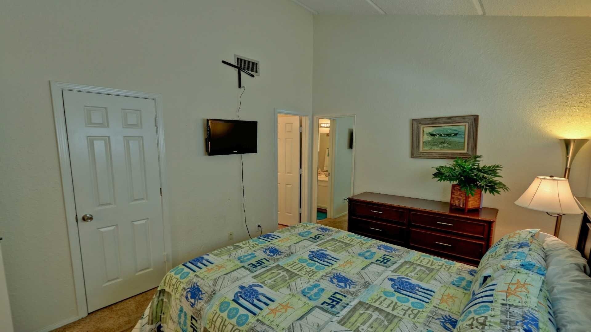 A bedroom with a bed, dresser, TV, and a door.
