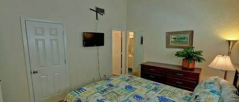 A bedroom with a bed, dresser, TV, and a door.
