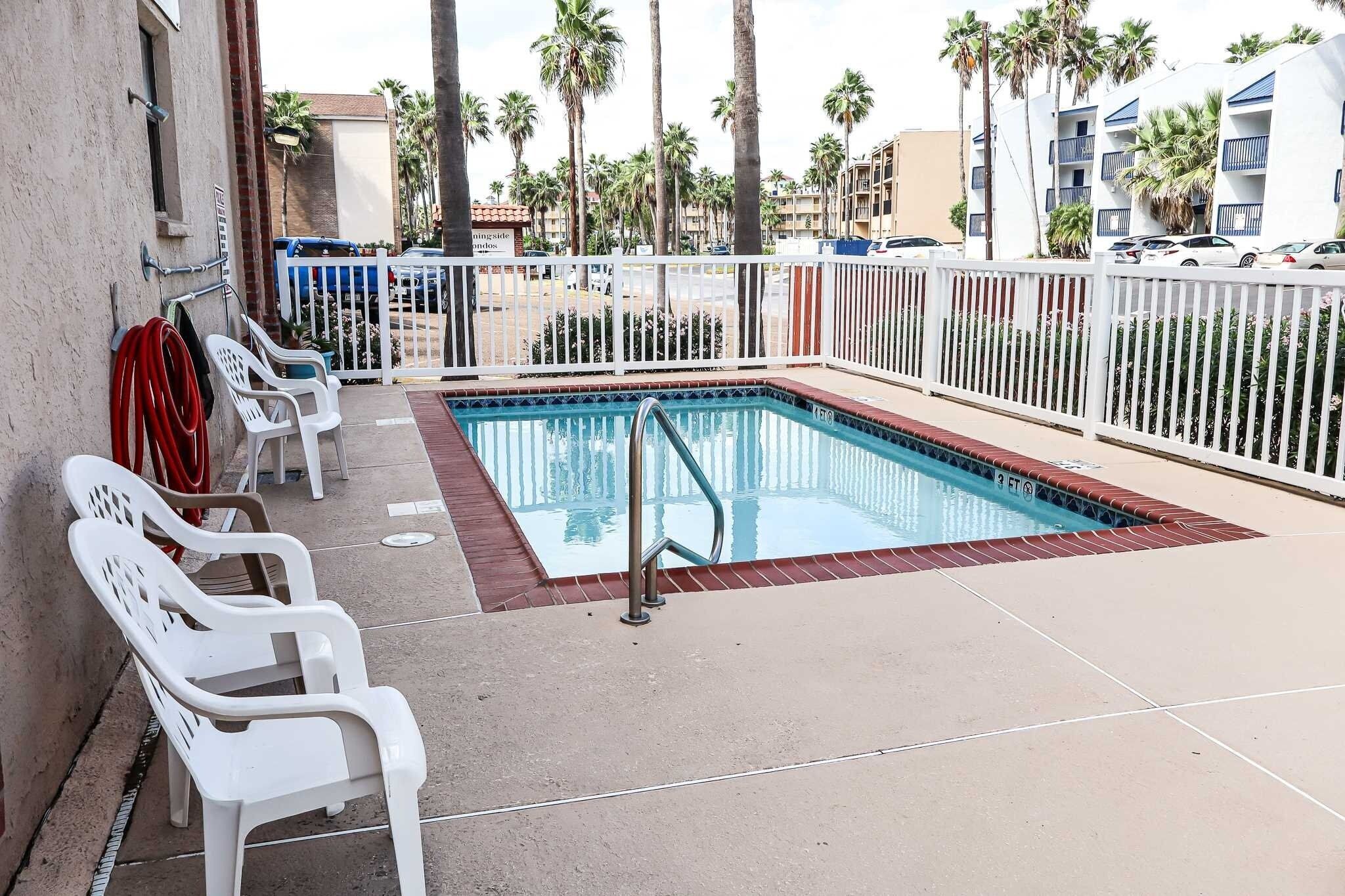 A swimming pool with a metal ladder, white plastic chairs, and a white fence.