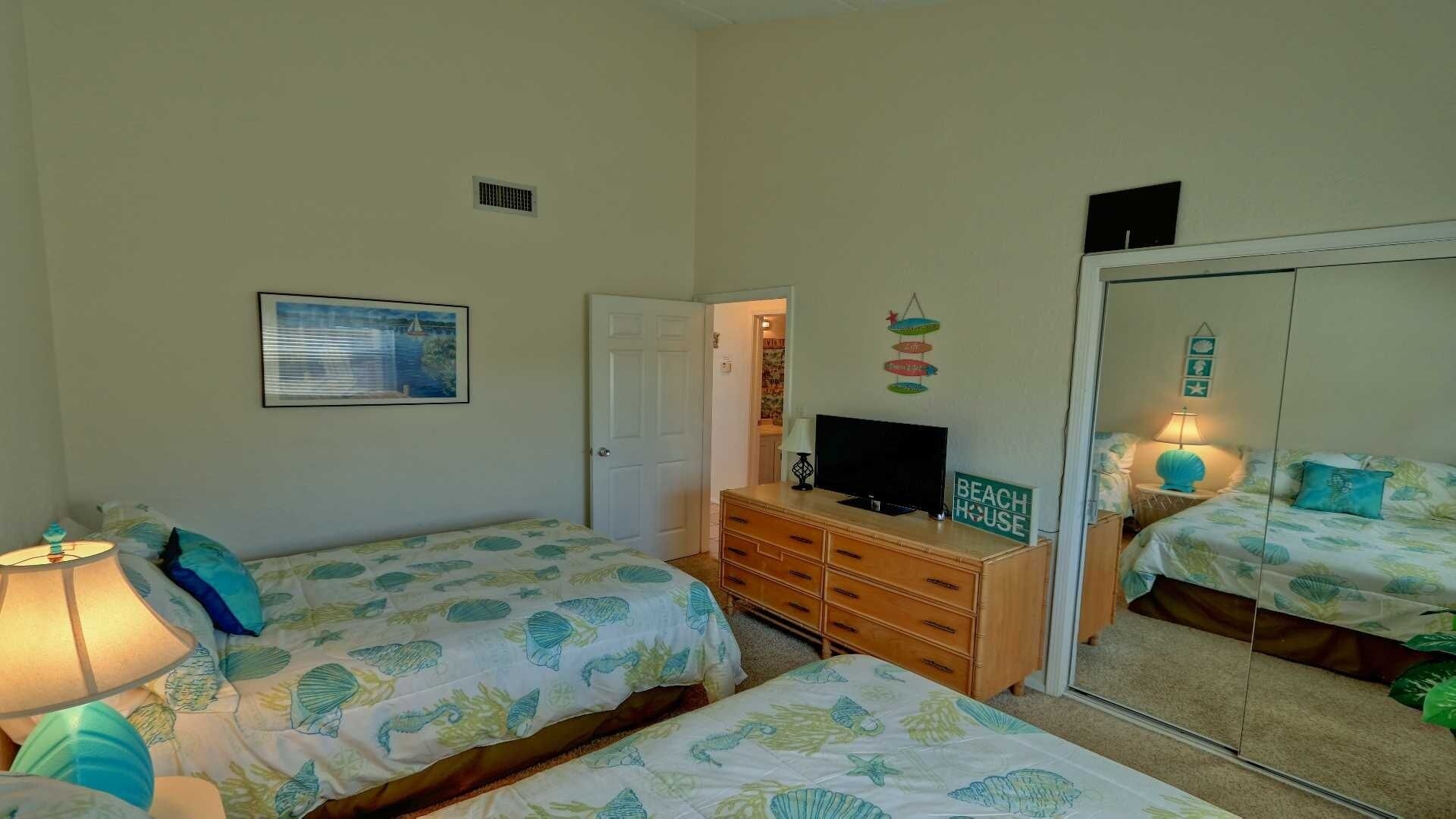 A bedroom with two beds, a dresser, a television, and a mirror.