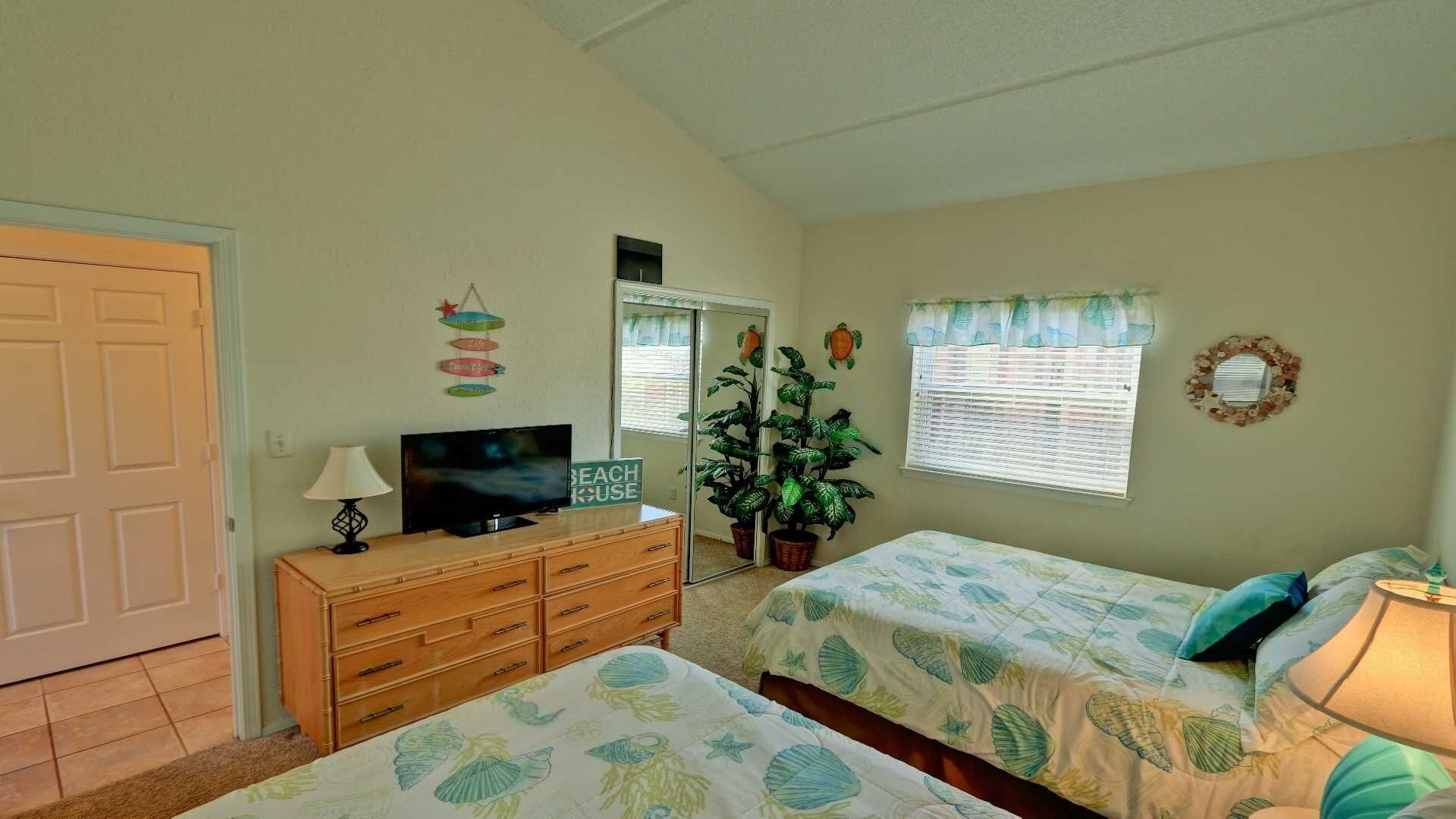 A bedroom with two beds, a TV, a dresser, and a potted plant.