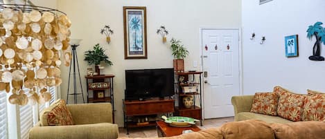 A living room with a television, sofas, a coffee table, and decorative plants.