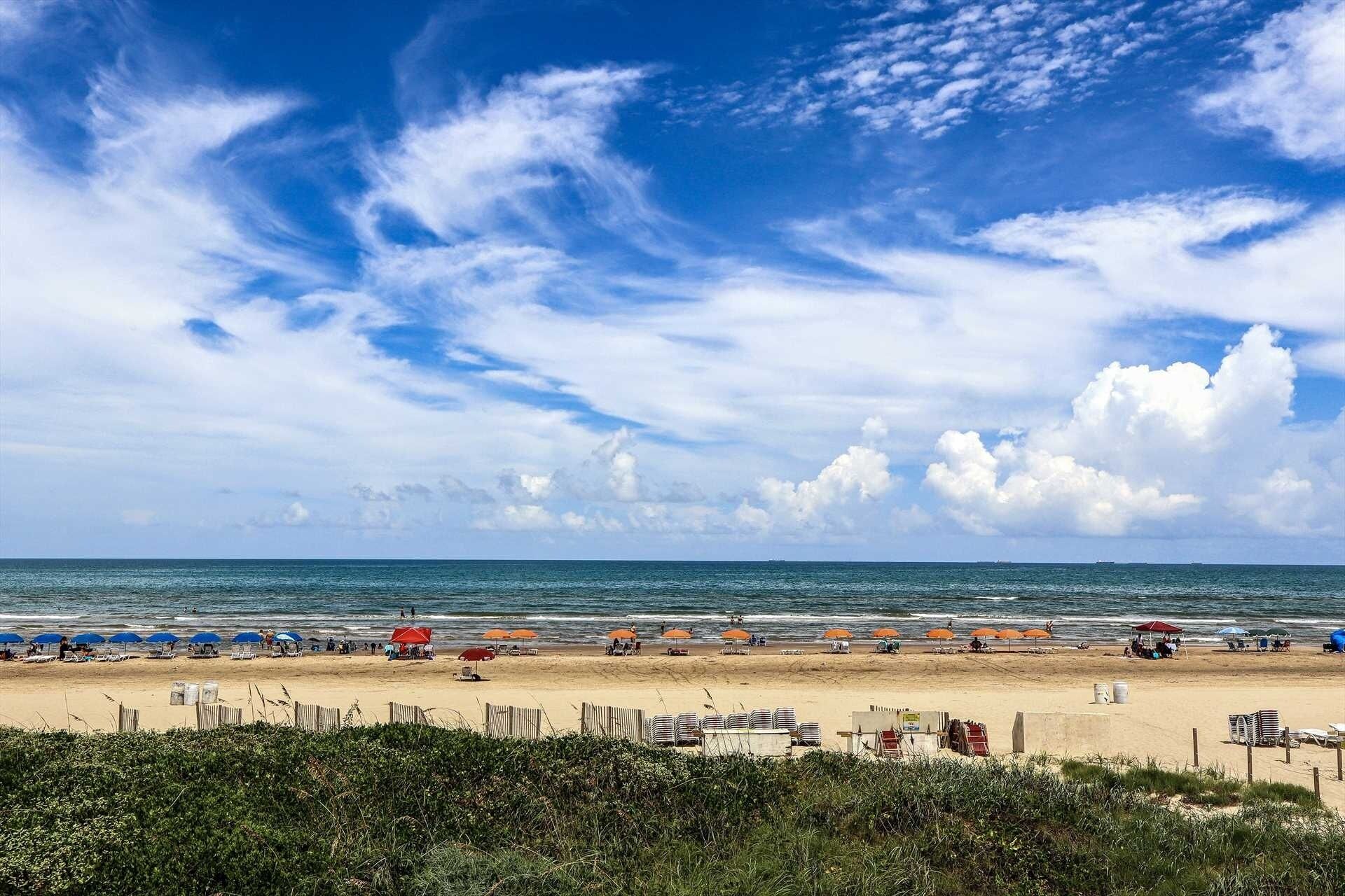 Una playa con sombrillas, sillas de playa y una valla de madera.