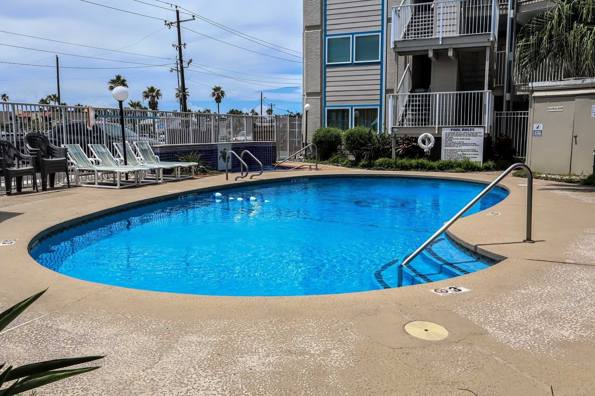A swimming pool surrounded by lounge chairs and a building with balconies.