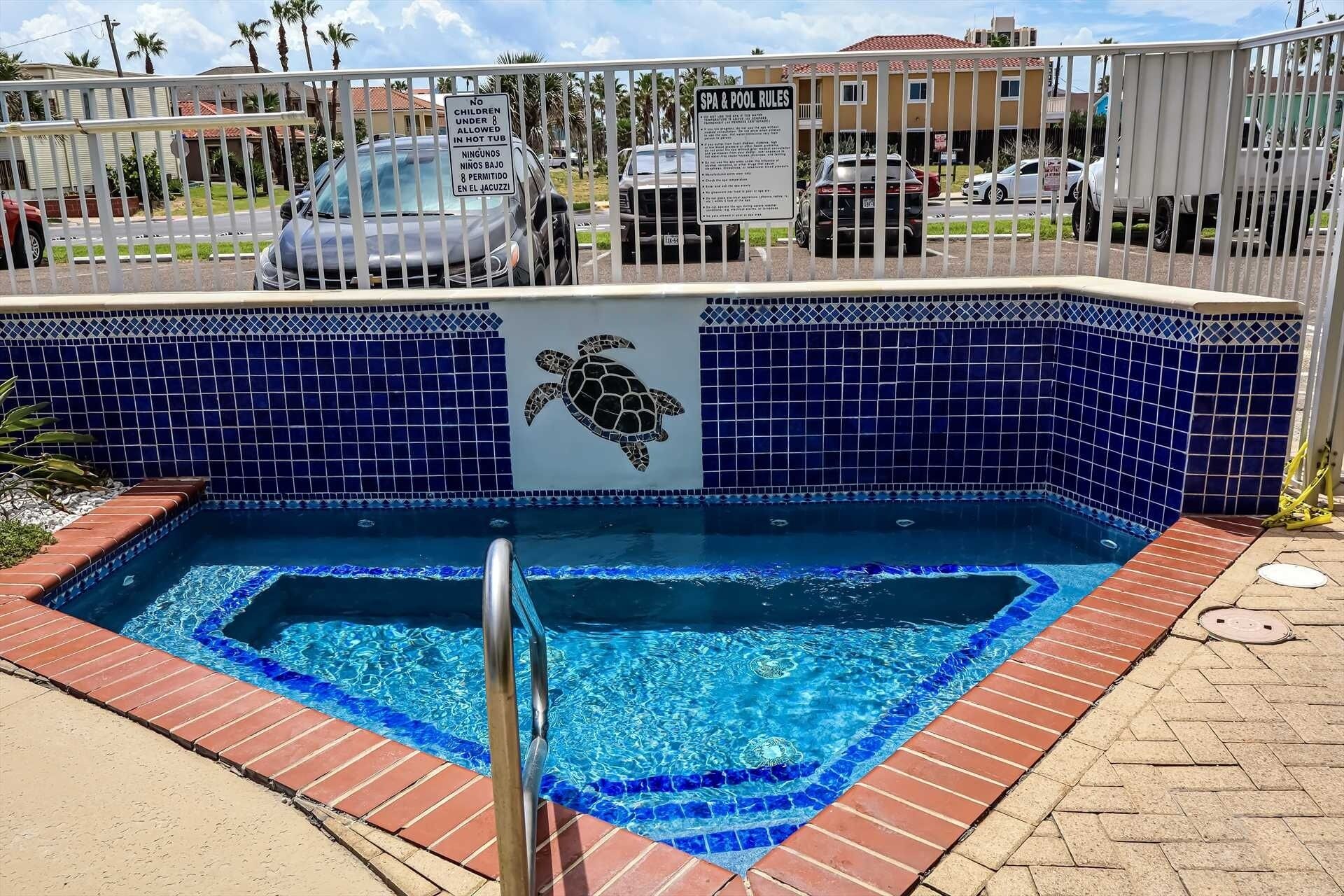 A small, rectangular hot tub with a turtle mosaic on the wall, surrounded by a metal fence.