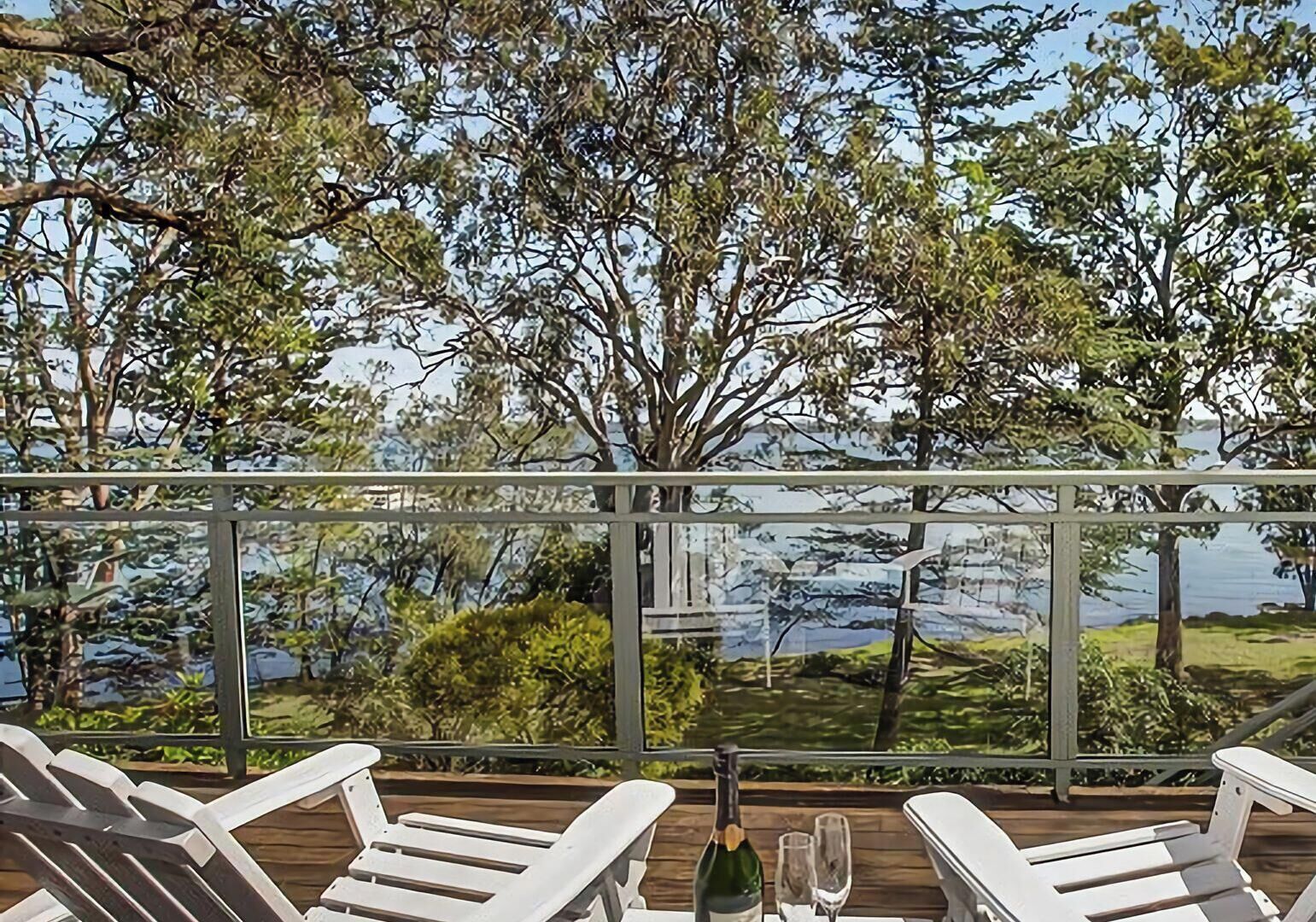 Eine Terrasse mit weißen Stühlen und einem Tisch, mit Blick auf ein Gewässer und Bäume.