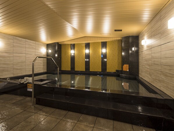 Una piscina interior moderna con suelo y paredes negras, techo de madera y un panel mural amarillo.