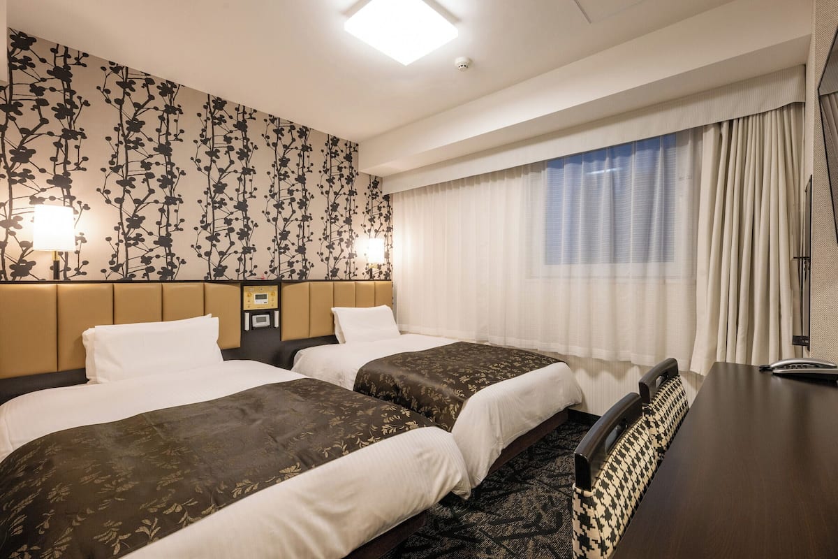 A hotel room with two beds, a desk, a telephone, and a window with curtains.