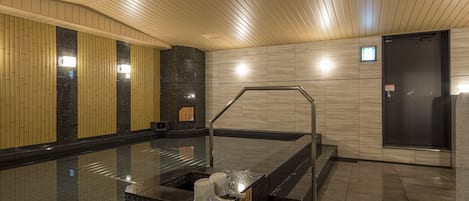 Et moderne poolområde indendørs med glasafskærmning, gelænder i metal og en sort dør.