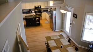 A modern kitchen with white cabinets, a black countertop, a stainless steel refrigerator, and a ceiling fan.