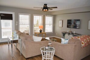 Een woonkamer met een bank, een salontafel, een lamp, een televisie en een plafondventilator.