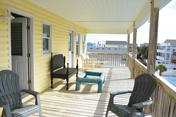 A covered porch with a wooden deck, a bench, two Adirondack chairs, and a small table.