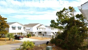 A row of white single-story houses with attached porches, a gravel driveway, and a small parking area.