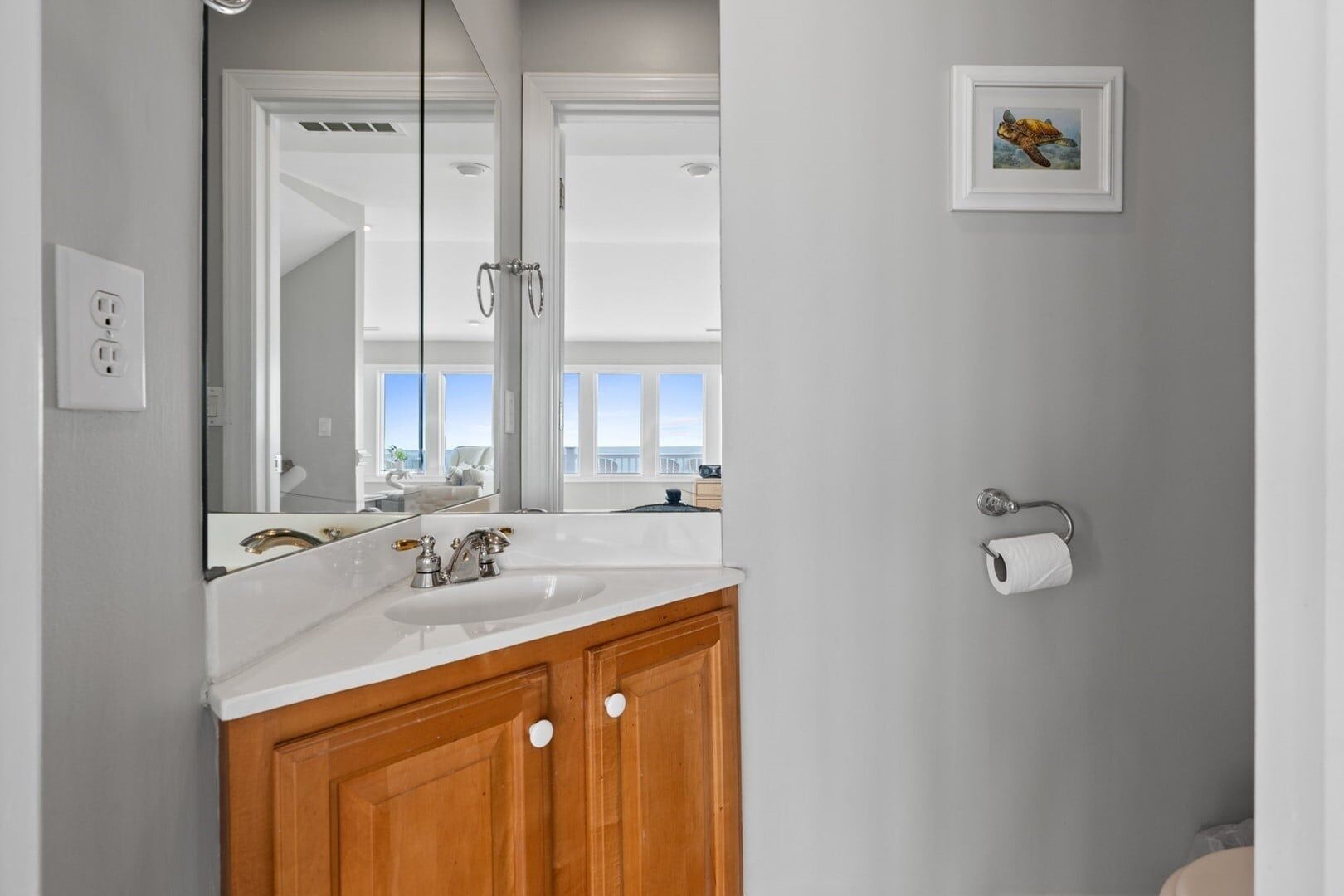 A bathroom with a white sink, wooden cabinets, a mirror, and a framed picture on the wall.