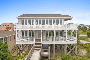 A two-story beachfront house with a balcony, a deck, and a covered outdoor area.