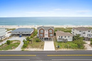 A coastal residential area with beachfront properties, a road in the foreground, and a clear view of the ocean. - That's It 4 Bedroom Home by RedAwning (Supply)