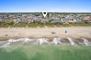 Eine Küstenwohngegend mit Häusern direkt am Strand, einem Sandstrand und ankommenden Wellen.
