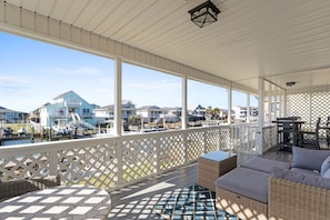 Un espacio al aire libre techado con vistas a barcos y casas, muebles de mimbre y un suelo estampado.