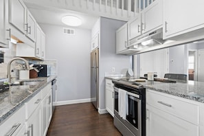 Eine moderne Küche mit weißen Schränken, Granit Arbeitsplatten, einem eingebauten Ofen und einem Edelstahl-Kühlschrank.