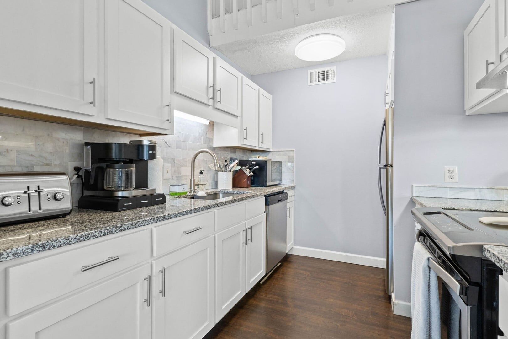 A modern kitchen with white cabinets, a built-in oven, a coffee maker, and a dishwasher.