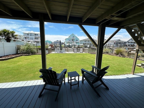A covered deck with two Adirondack chairs and a small table, overlooking a grassy yard and a residential area with houses.