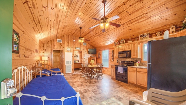 L’intérieur d’une cabane en rondins comprend un lit, une table à manger, des chaises, un coin cuisine et un ventilateur de plafond.