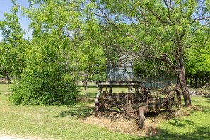 An old, rustic wooden structure with a large wheel and a chimney, surrounded by lush green trees. - Sunflower Rr9122sf 1 Bedroom Home by RedAwning (New Braunfels)