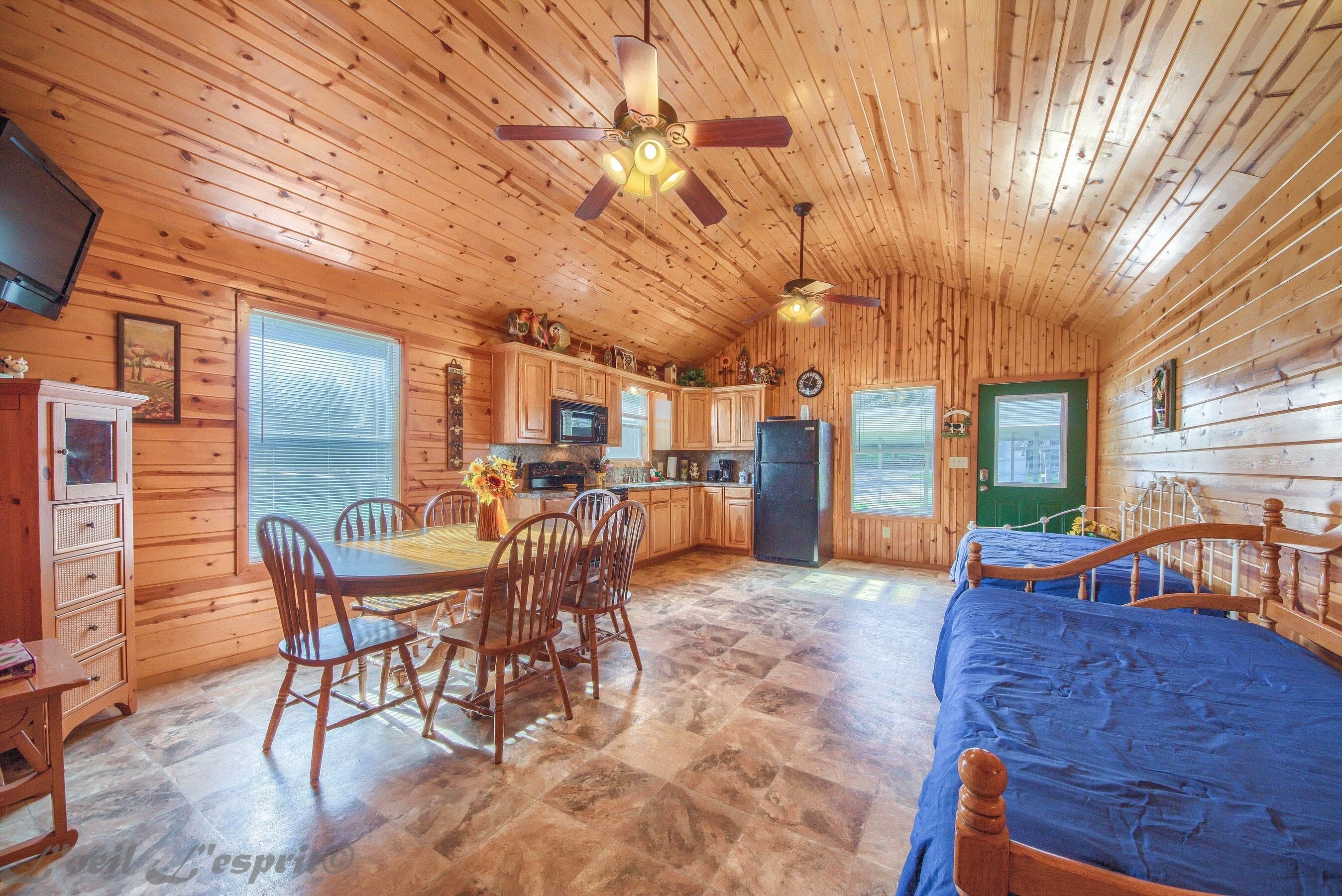A wooden cabin interior with a dining area, kitchen, and a bed.