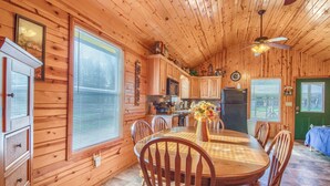 L’intérieur d’une cabane en bois comprend une table à manger, des chaises, un coin cuisine et un ventilateur de plafond.