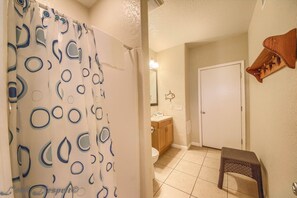 A bathroom with a shower curtain, a toilet, a sink, and a small stool.