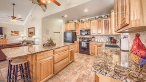 A kitchen with wooden cabinets, granite countertops, a ceiling fan, and a microwave. - Cowboy Lodge Rr94404 #4 4 Bedroom Home by RedAwning (New Braunfels)