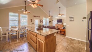 A spacious kitchen with a large island, wooden cabinets, and ceiling fans. There are multiple windows providing natural light and a view of the outdoors. - Cowboy Lodge Rr94404 #4 4 Bedroom Home by RedAwning (New Braunfels)