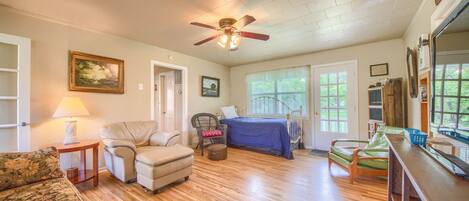 A spacious room with hardwood floors, a ceiling fan, a bed with a blue bedspread, a wooden desk, and a chair.