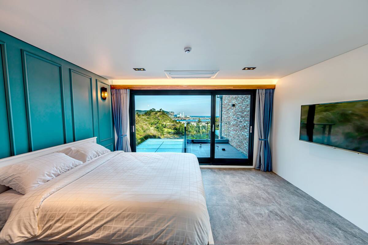 A bedroom with a bed, a view of the outdoors, a sliding glass door, and a mounted TV.