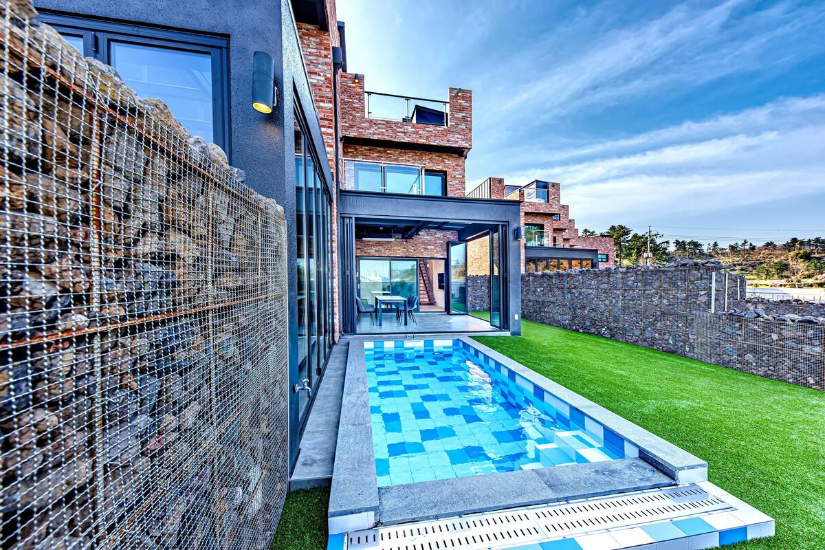 A modern house with a swimming pool, a covered patio, and a stone wall.
