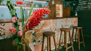 A bar area with a floral arrangement in a vase, wooden stools, and a patterned wall. - Drifter Hostel (São Sebastião)