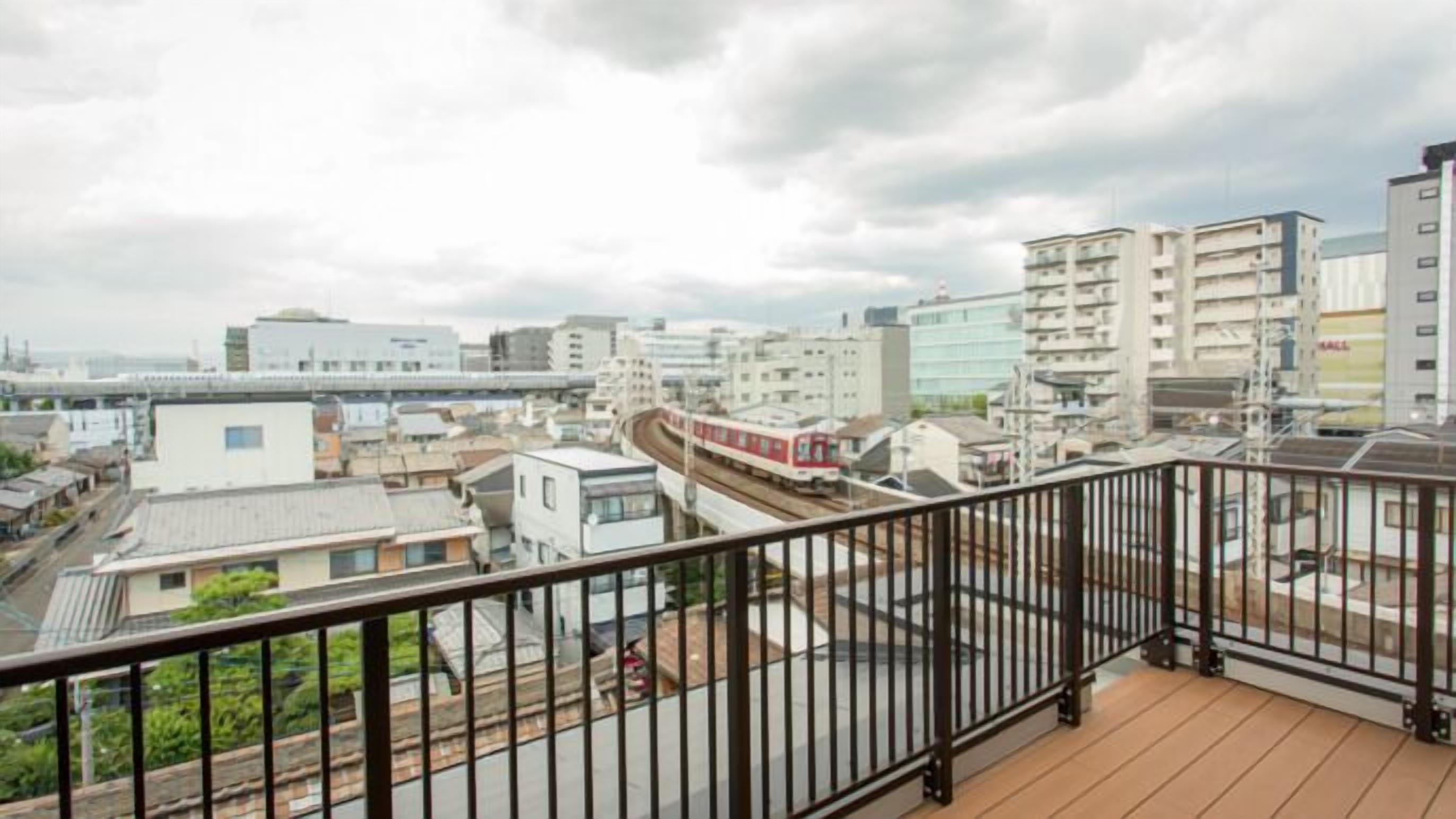 A cityscape with modern buildings, a train track, and a balcony with a metal railing.