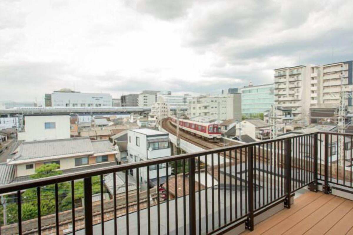 A cityscape with modern buildings, a train track, and a balcony with a metal railing.