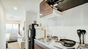 Une cuisine moderne équipée d’un réfrigérateur, d’une cuisinière et d’un évier. La pièce adjacente comprend un lit et une fenêtre.