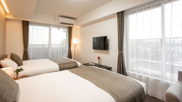 Une chambre d’hôtel avec deux lits, une télévision, une fenêtre avec des rideaux et un appareil de climatisation.