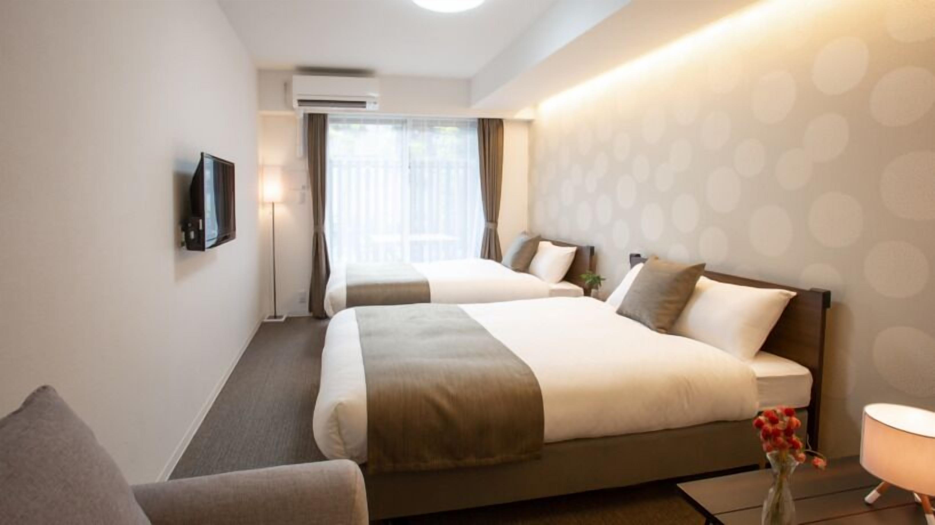 A hotel room with two beds, a TV, a desk, and a window with curtains.