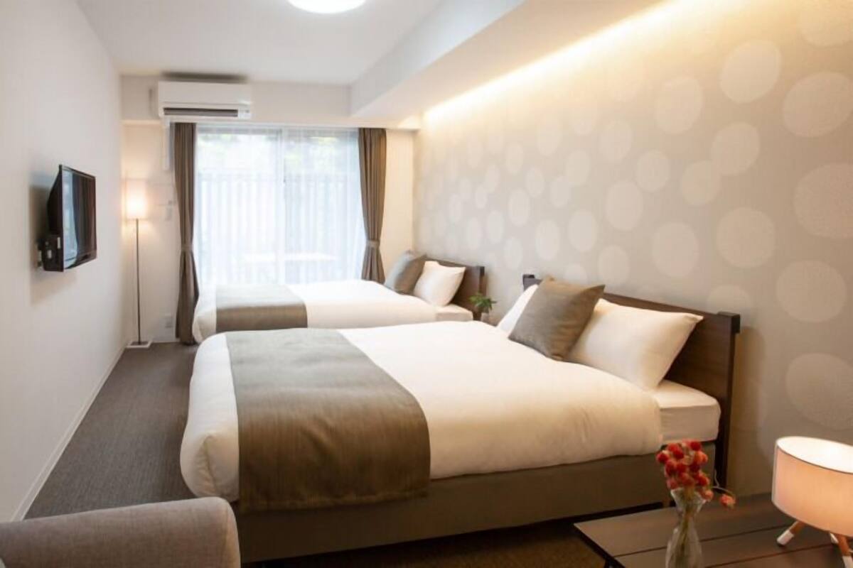 A hotel room with two beds, a TV, a desk, and a window with curtains.