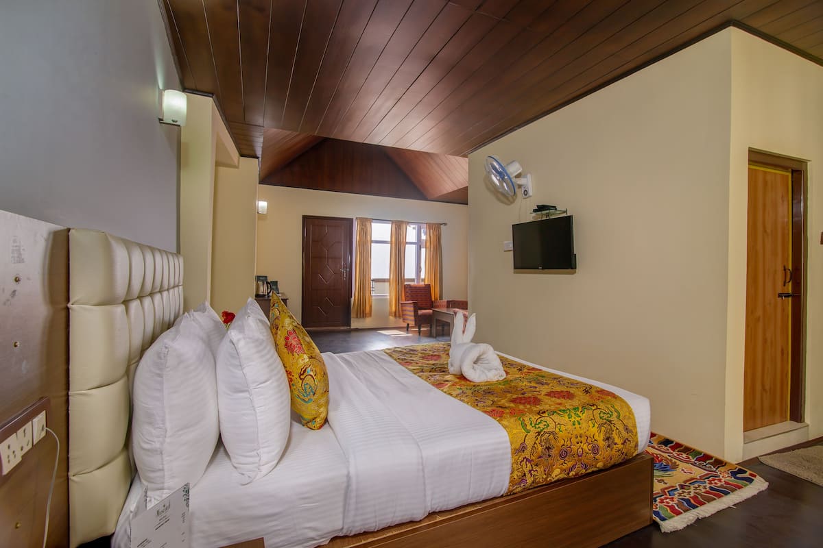 Habitación de hotel con una cama grande, techo de madera, televisión y vista al pasillo.