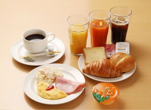 Aamiaispöytä, jolla on lautanen täynnä munia, kinkkua, croissantteja, paahtoleipää ja mehua.