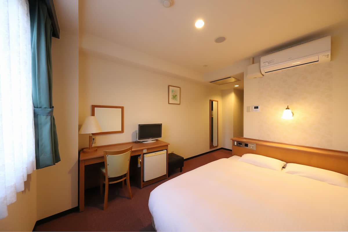 Een hotelkamer met een bed, een bureau met computer, een stoel en een kleine koelkast.