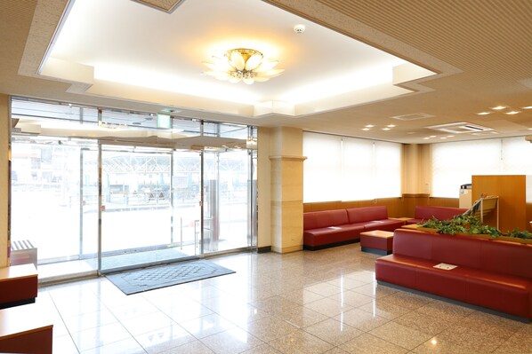A hotel lobby with a reception desk, a red seating area, and a large glass door leading outside.