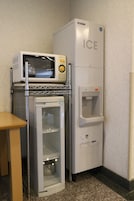Una kitchenette compacta con microondas, refrigerador y dispensador de agua.
