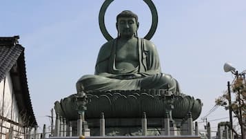 Una gran estatua de Buda con un halo, sentado sobre un pedestal de loto, rodeado de arquitectura tradicional.