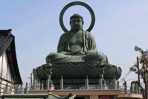 A large Buddha statue with a halo, seated on a lotus base, surrounded by traditional architecture.
